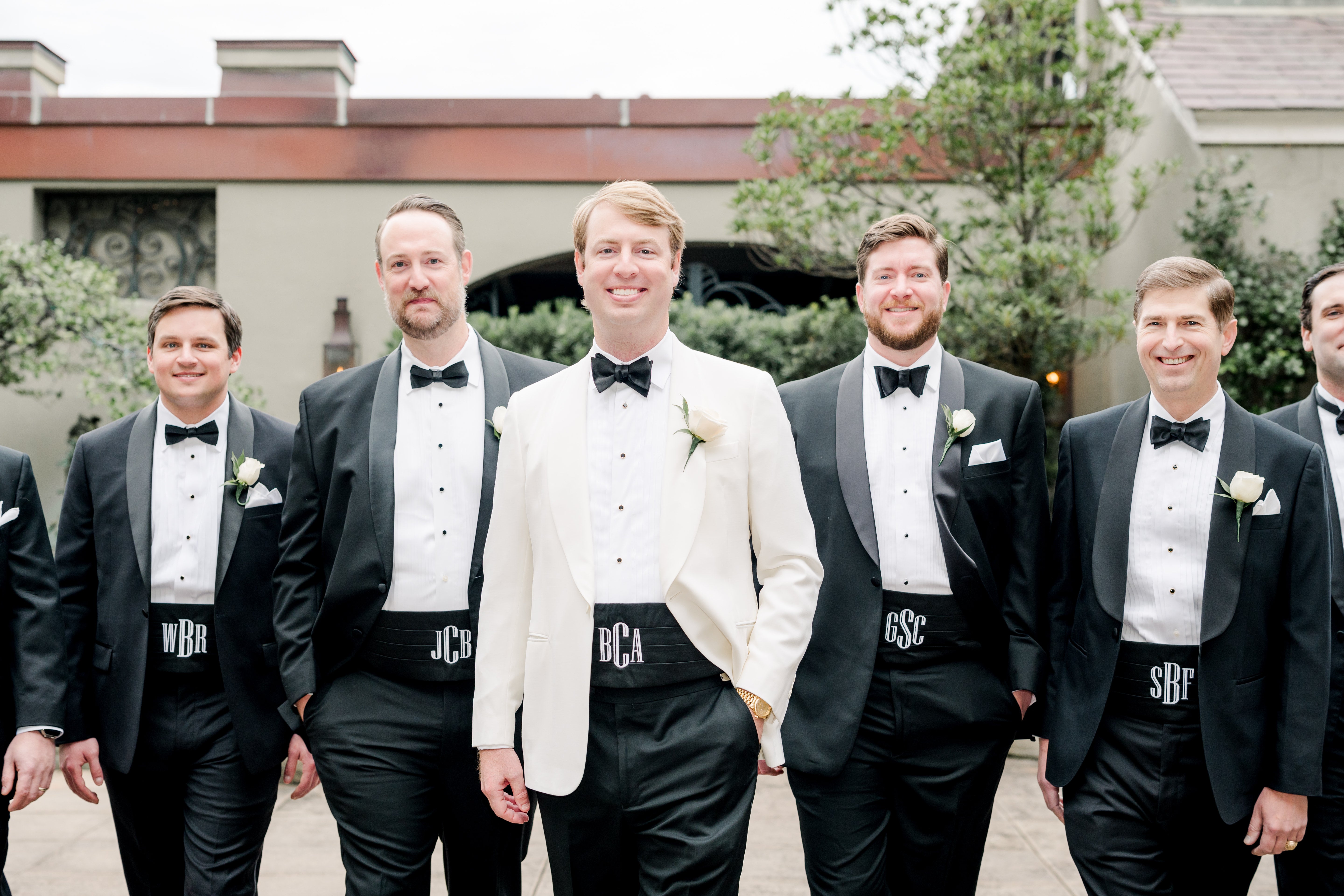 Groom in white dinner jacket and groomsmen in black tuxedos with monogrammed cummerbunds