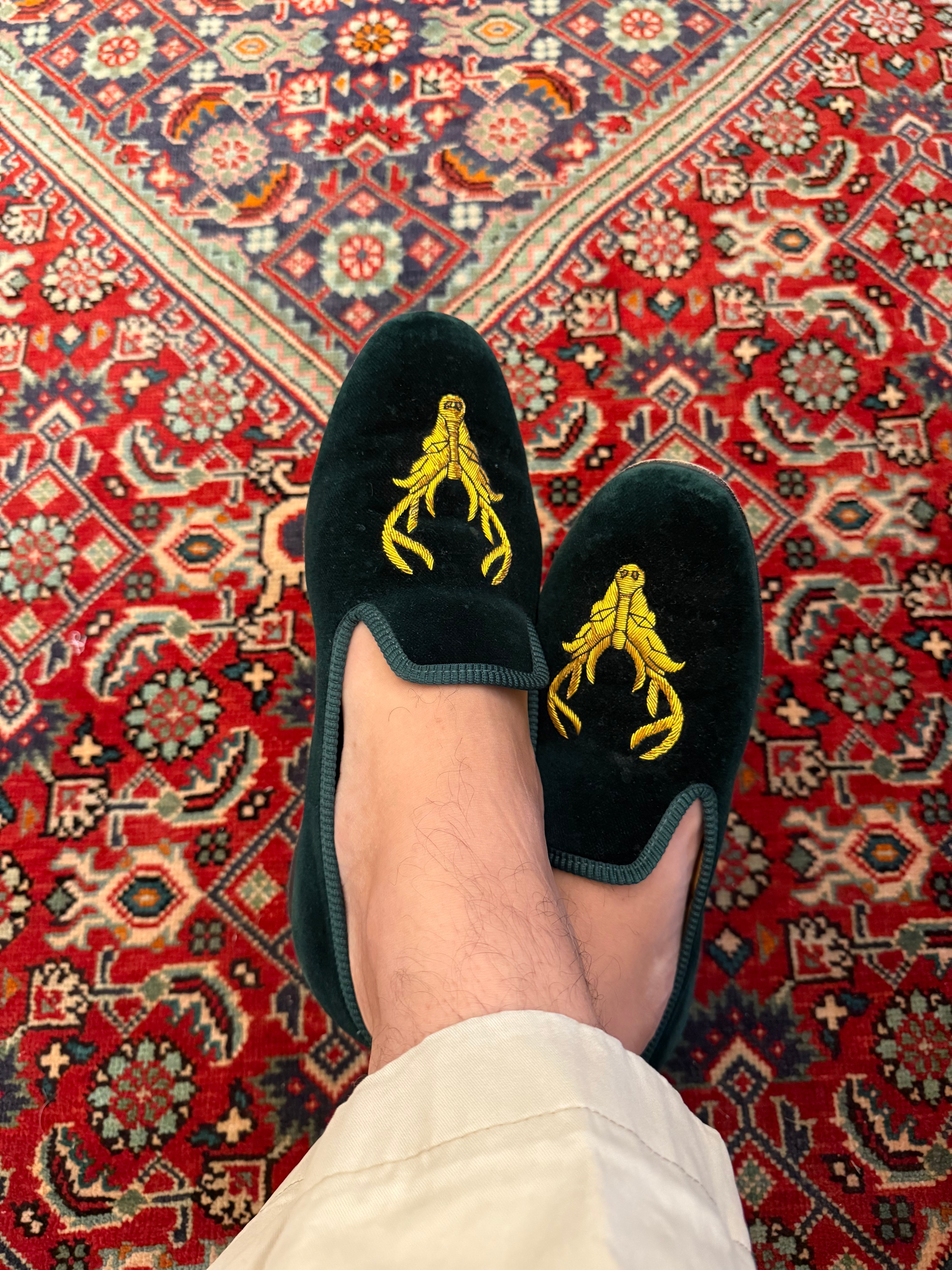 Velvet Albert Slippers with gold stag on green velvet, against red Persian rug