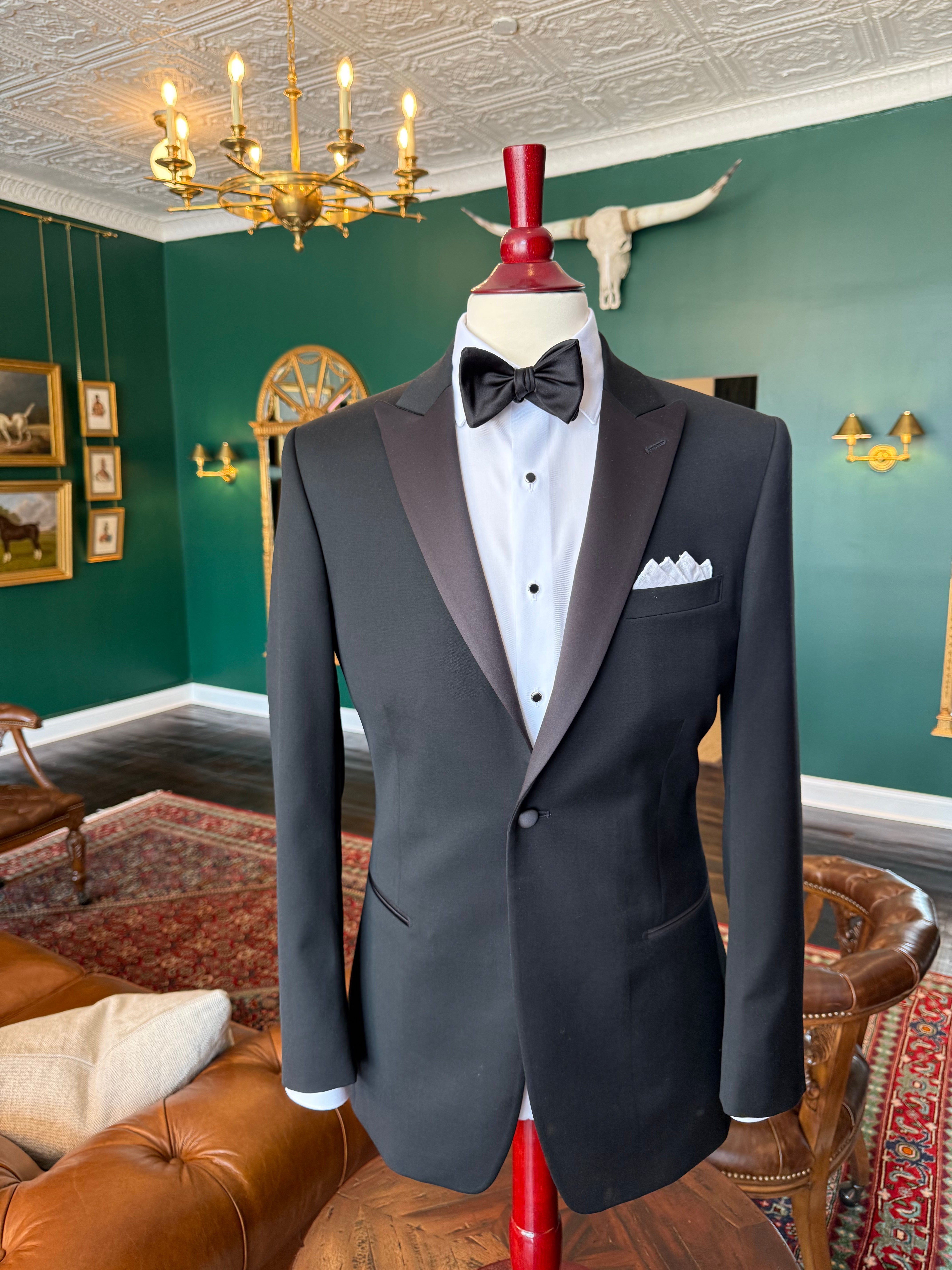 Classic black peak lapel tuxedo with satin facing on mahogany mannequin, available for rent at Waring Tuxedos in Fort Worth.