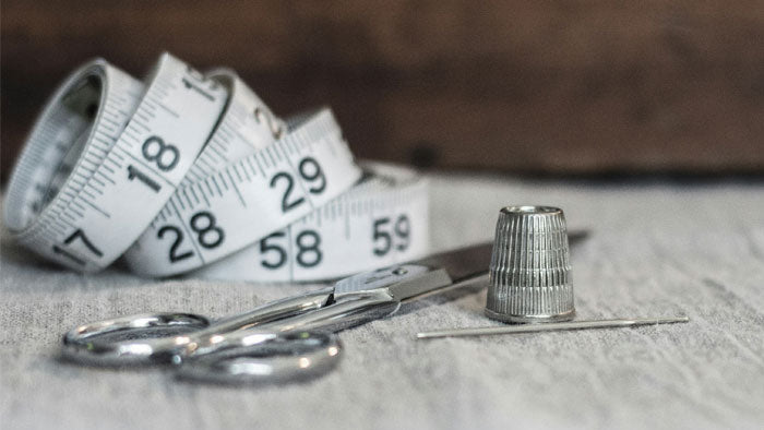 Stock photo of tailor tools - scissors, tape measure, needle, and thimble.