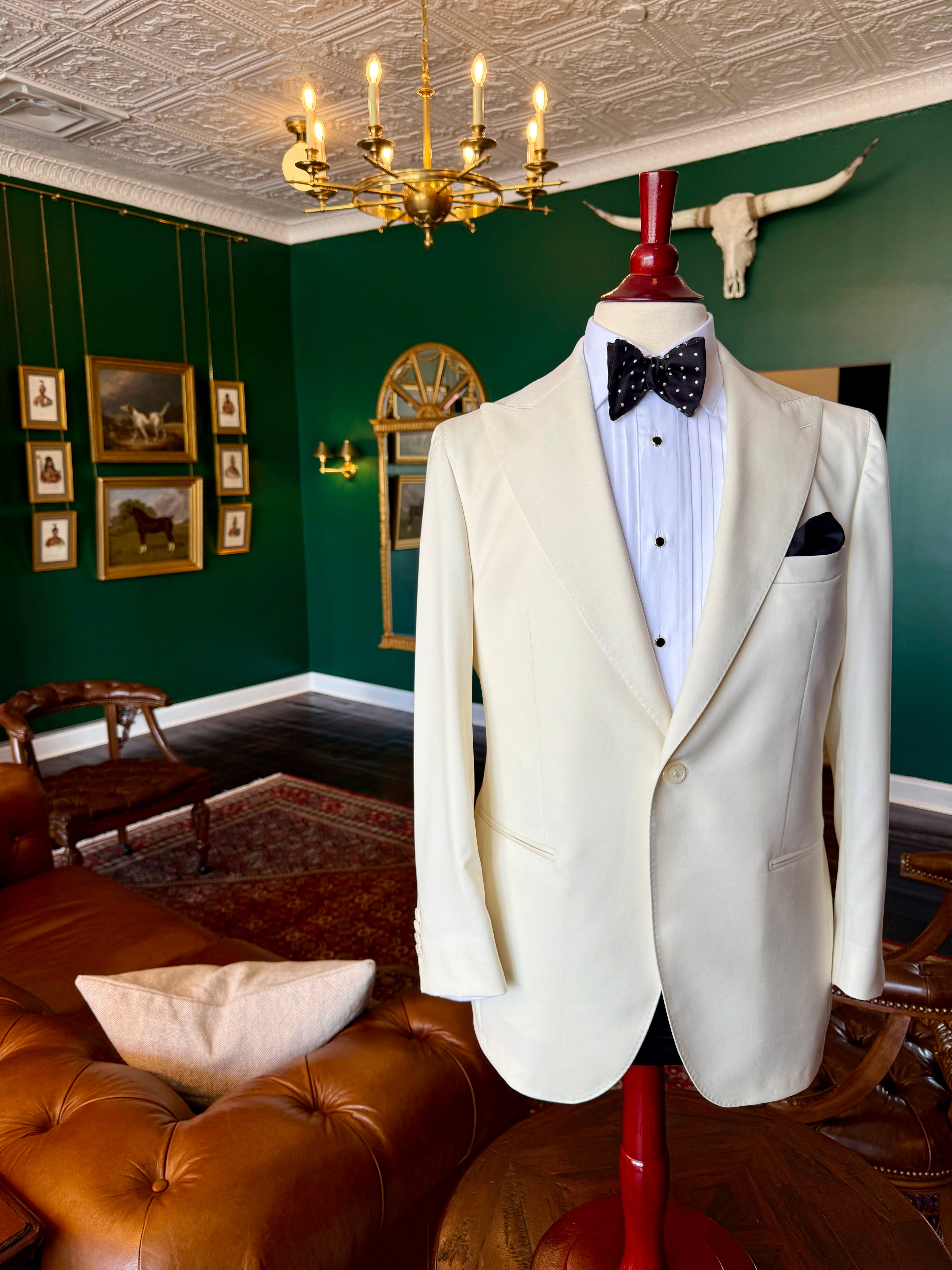Custom ivory dinner jacket with peak lapel by Waring Tuxedos, displayed on a mahogany mannequin in our Fort Worth tailor shop with green walls and oil paintings.