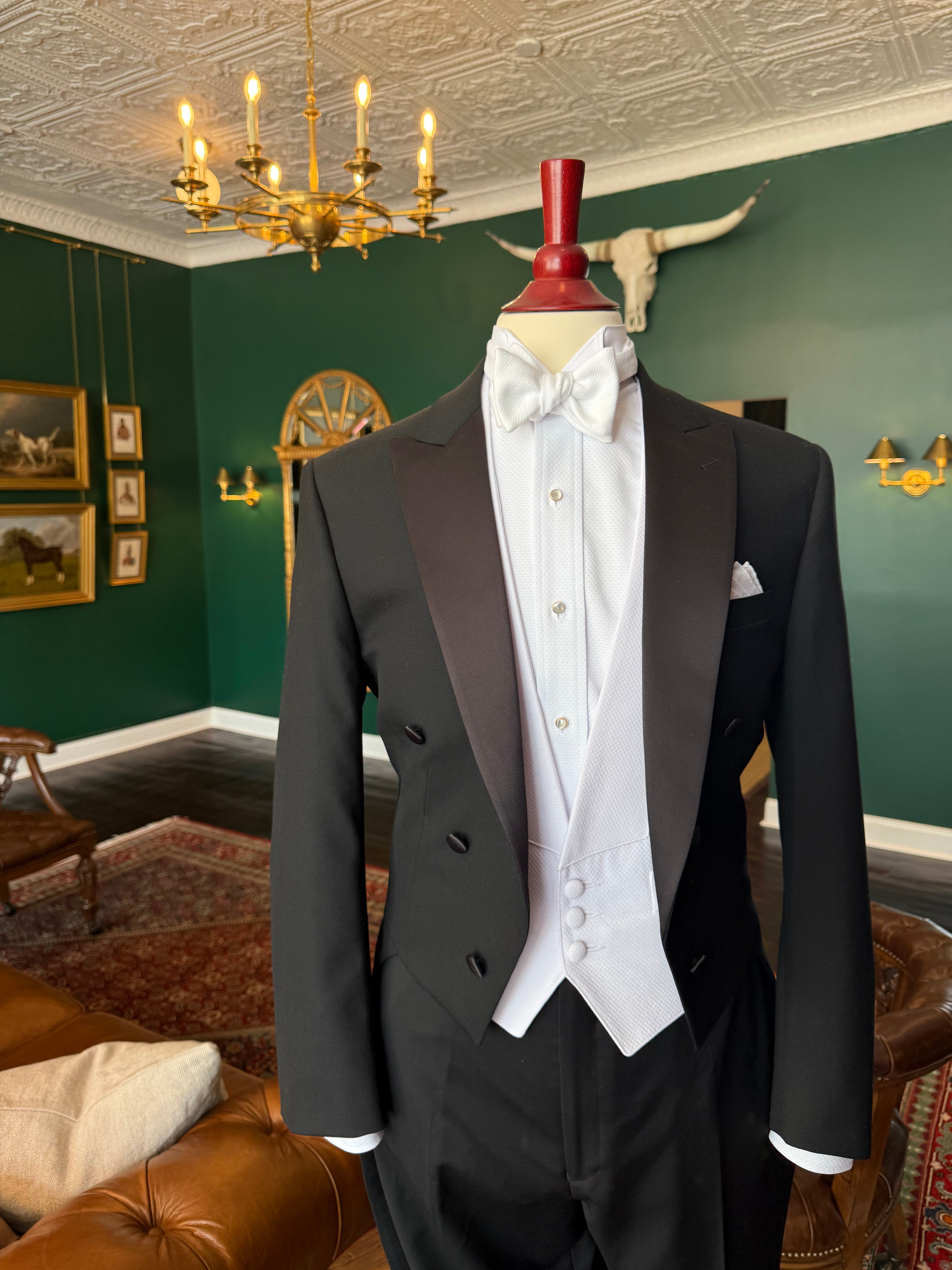 White tie and tails tuxedo on mahogany mannequin in Waring Tuxedos, against background of green walls, oil paintings, and a club vibes in traditional tailor shop.